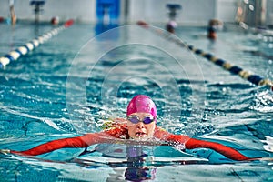 Female athlete in a red-yellow swimsuit is swimming in the style of breaststroke.