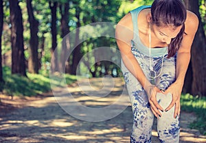 Female athlete runner touching knee in pain, fitness woman running in park.