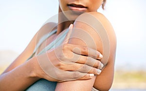 Female athlete suffering from shoulder pain while training outdoors. Fit woman holding her painful arm while exercising