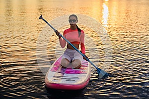 Female athlete swimming on sup board with paddle in hands.