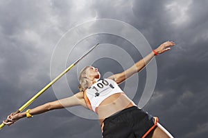 Female athlete throwing javelin against cloudy sky low angle view