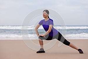 Female athlete warming up and stretching the legs before running at the beach