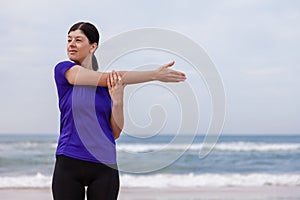 Female athlete warming up and stretching the upper body before running at the beach