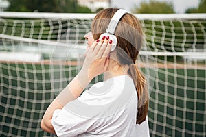 Female athlete with white headphones at the stadium near the football goal.
