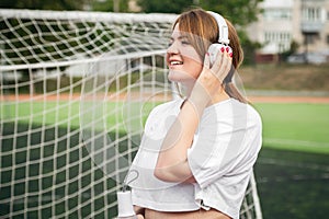 Female athlete with white headphones at the stadium near the football goal.