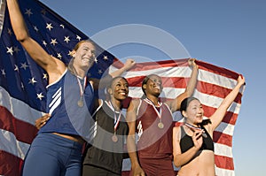 Female Athletes Holding American Flag Against Blue Sky
