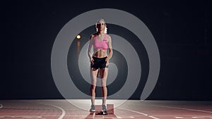 Female athletes warming up at running track before a race. In slow motion. Woman runner at athletics track crouching at