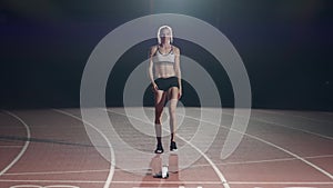 Female athletes warming up at running track before a race. In slow motion. Woman runner at athletics track crouching at