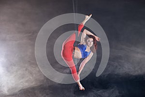 Female athletic, sexy and flexible aerial circus artist with redhead on aerial straps on black background