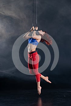 Female athletic, sexy and flexible aerial circus artist with redhead on aerial straps on black background