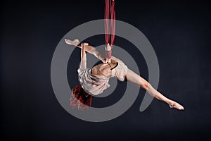 Female athletic, sexy and flexible aerial circus artist with redhead dancing in the air on the silk