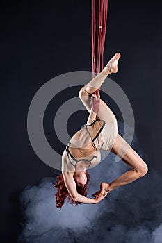 Female athletic, sexy and flexible aerial circus artist with redhead dancing in the air on the silk