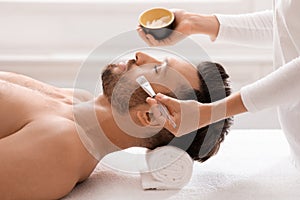 Female attendant applying nourishing face mask on sleeping man face