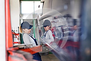 Female auto mechanic changing tieres in auto service. Beautiful woman holding tire in a garage, wearing blue coveralls.