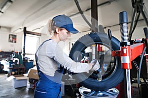 Female auto mechanic changing tieres in auto service. Beautiful woman holding tire in a garage, wearing blue coveralls. photo