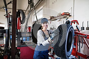 Female auto mechanic changing tieres in auto service. Beautiful woman holding tire in a garage, wearing blue coveralls. photo
