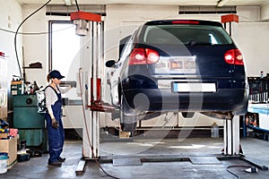 Female auto mechanic elevating car on car lift, working underneath. Beautiful woman working in a garage, wearing blue