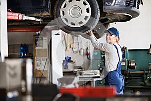 Female auto mechanic elevating car on car lift, working underneath. Beautiful woman working in a garage, wearing blue