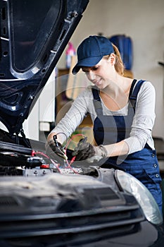 Female auto mechanic repairing, maintaining car, car battery. Beautiful woman working in a garage, wearing blue photo