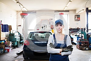 Female auto mechanic repairing, maintaining car. Beautiful woman standing in a garage, wearing blue coveralls. photo