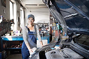 Female auto mechanic repairing, maintaining car. Beautiful woman standing in a garage, wearing blue coveralls. photo