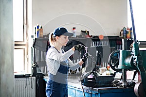 Female auto mechanic repairing, maintaining car. Beautiful woman working in a garage, wearing blue coveralls. photo