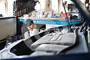Female auto mechanic repairing, maintaining car. Beautiful woman working in a garage, wearing blue coveralls. photo