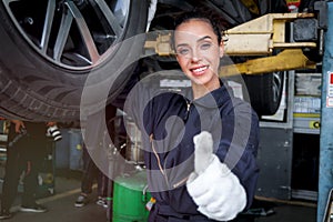 Female auto mechanic work in garage, car service technician woman give thumb up, repair customer car at automobile service center