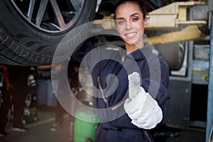 Female auto mechanic work in garage, car service technician woman give thumb up, repair customer car at automobile service center