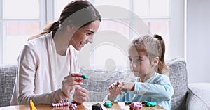 Female babysitter helping cute kid girl sculpting play dough together