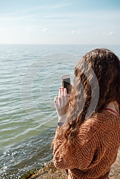Female from the back filming video or making a picture on the beach using her smartphone