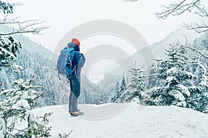 Žena batohem s batohem oblečená teplá péřová bunda se těší zasněžené horské krajiny, zatímco ona trekking zimní hory