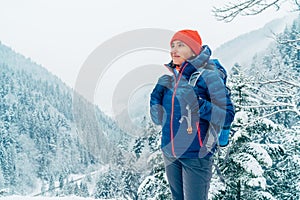Žena batohom s batohom oblečená teplá páperová bunda si užíva zasneženú horskú krajinu, zatiaľ čo ona chodí na zimné hory
