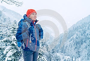 Žena batohem s batohem oblečená teplá péřová bunda se těší zasněžené horské krajiny, zatímco ona trekking zimní hory