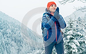 Žena Backpacker s batohom oblečená teplá páperová bunda otepľovanie dlane ruky a teší zasnežené hory krajiny, zatiaľ čo ona