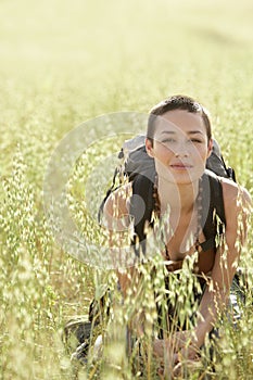 Female Backpacker Crouching In Field Of Grass