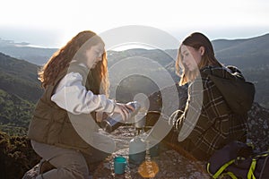 Female backpackers boiling tea water on camp stove outdoors