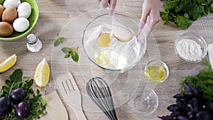 Female baker mixing egg with flour in bowl by wood spoon, cookies ingredients