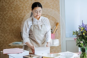 Female baker, pastry chef preparing cake order. Arabic Asian woman making cake for online delivery