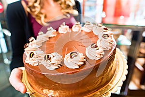 Female baker presenting cake in confectionery