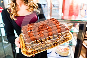 Female baker presenting cake in confectionery