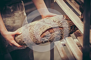 Female baker puts freshly baked bread on a wooden shelf