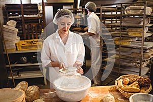 Female baker sifting flour through a sieve