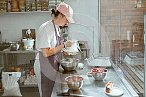 Female baker unwraps butter standing at metal counter with food products in shop