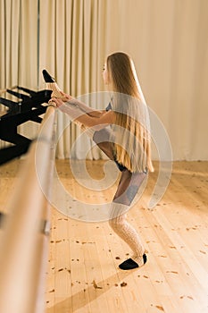 Female ballet dancer practicing at barre in dance studio - dance and ballerina concept