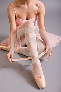 Female ballet dancer tying ribbon around ankle.