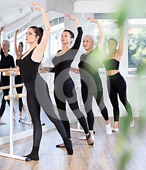 Female ballet trainer teaching group of dancers near ballet barre in dancing studio