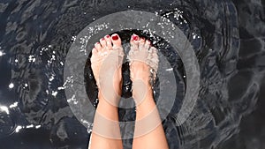 Female bare feet in clean water. Woman is splashing water with her feet in lake in slow motion