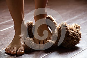 female bare feet stepping on a brown teddy bear on the old floor in a dark room, a toy on the floor with legs laid