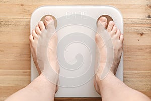 Female bare, hairy legs stand on smart scales that makes bioelectric impedance analysis, BIA, body fat measurement. Body